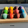 A wooden tray holds ten brightly colored, smooth spheres arranged in a row and a second row for sensory play.