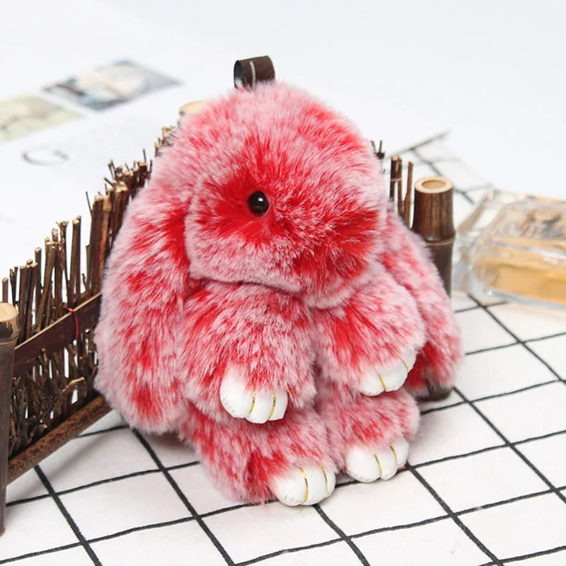 A fluffy red and white plush bunny keychain resting on a white grid surface.