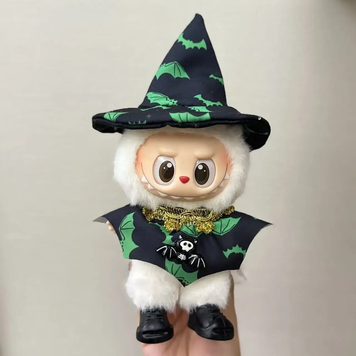 A cute doll wearing a witch costume with a black pointed hat and green bat patterns on a black dress.