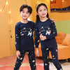 Two children wearing matching navy blue cotton pajama sets with an astronaut print