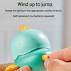Hands are rotating the spring of a teal wind-up animal toy to make it jump.
