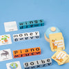 A collection of wooden letter blocks and cards for a Montessori word spelling game including wings, money, piano, and globe.