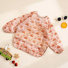 A pink waterproof long sleeve feeding bib patterned with rainbows and hearts lying on a light surface.
