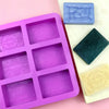 A purple silicone soap mold with six cavities and a green square mold are displayed on a white surface.