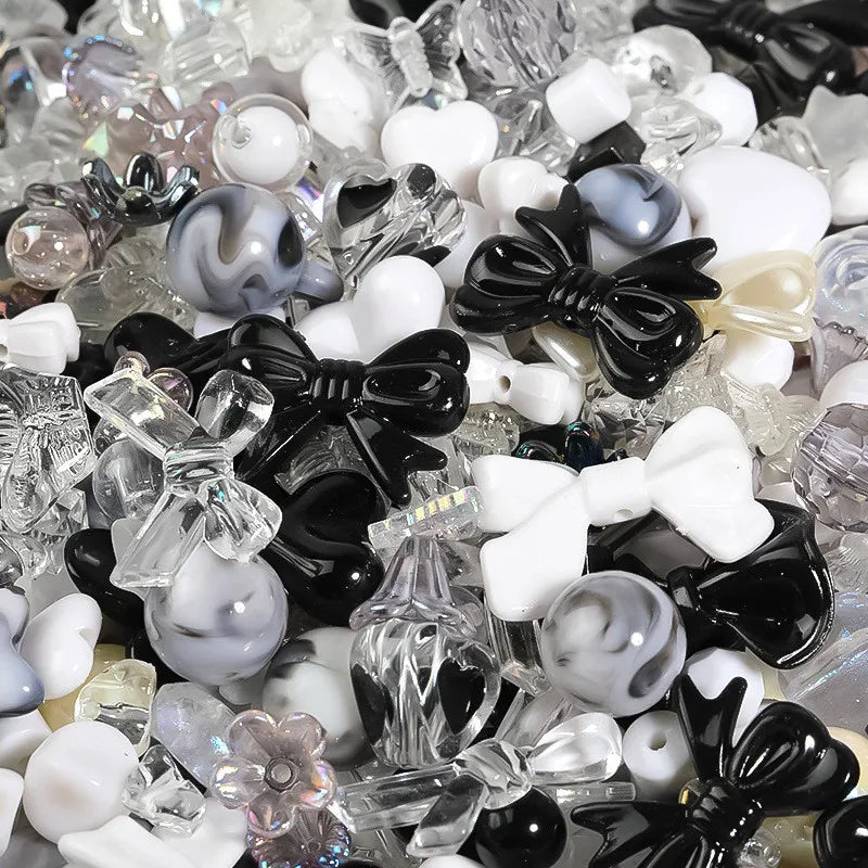 A close-up view of mixed clear and colored acrylic loose beads for jewelry making, including white, black, and iridescent pie