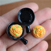 A hand holds a miniature dollhouse beef steak and pasta set toy food with an orange-colored item.