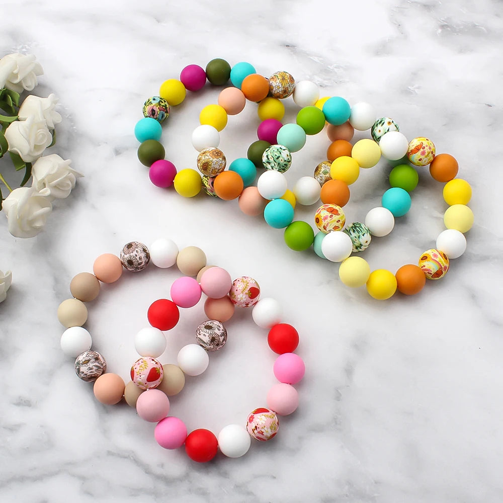 A collection of colorful printed silicone beads in leopard and daisy patterns arranged in circular shapes on a white marble s