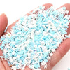 A handful of polymer clay slices in light blue and white snowflake designs is held in a hand.