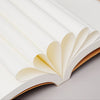 A close-up of a white kraft paper notebook with pages visible, showing the binding and blank interior.