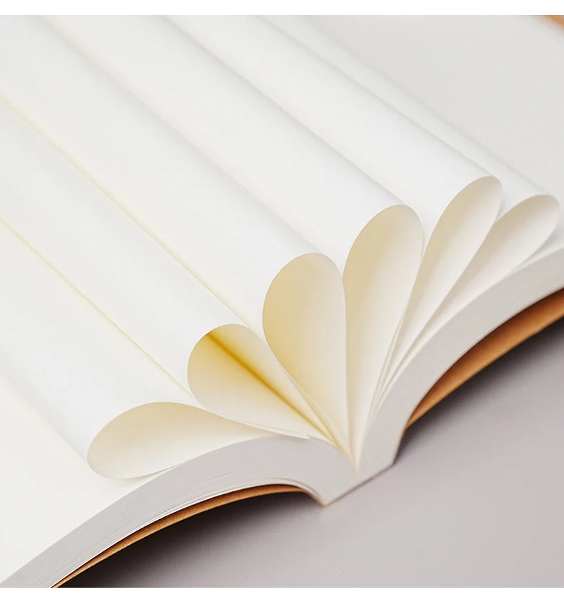 A close-up of a white kraft paper notebook with pages visible, showing the binding and blank interior.