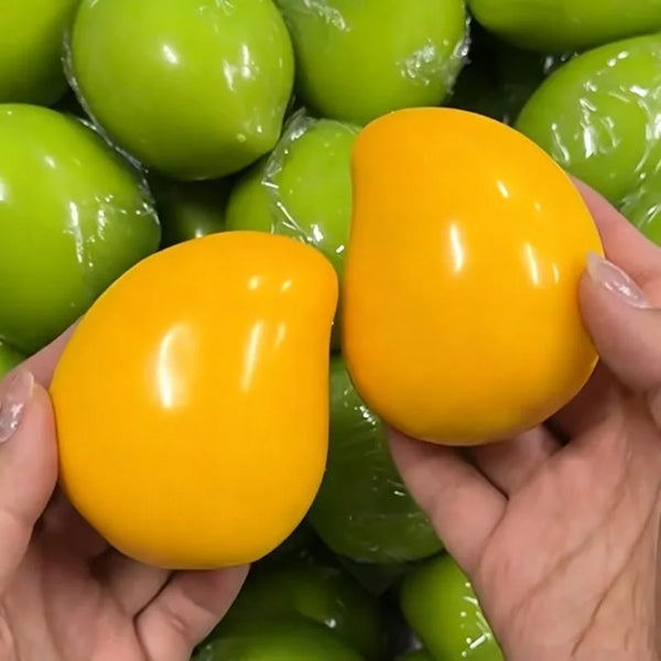 A hand holds a bright orange mango squeeze stress ball among green ones.