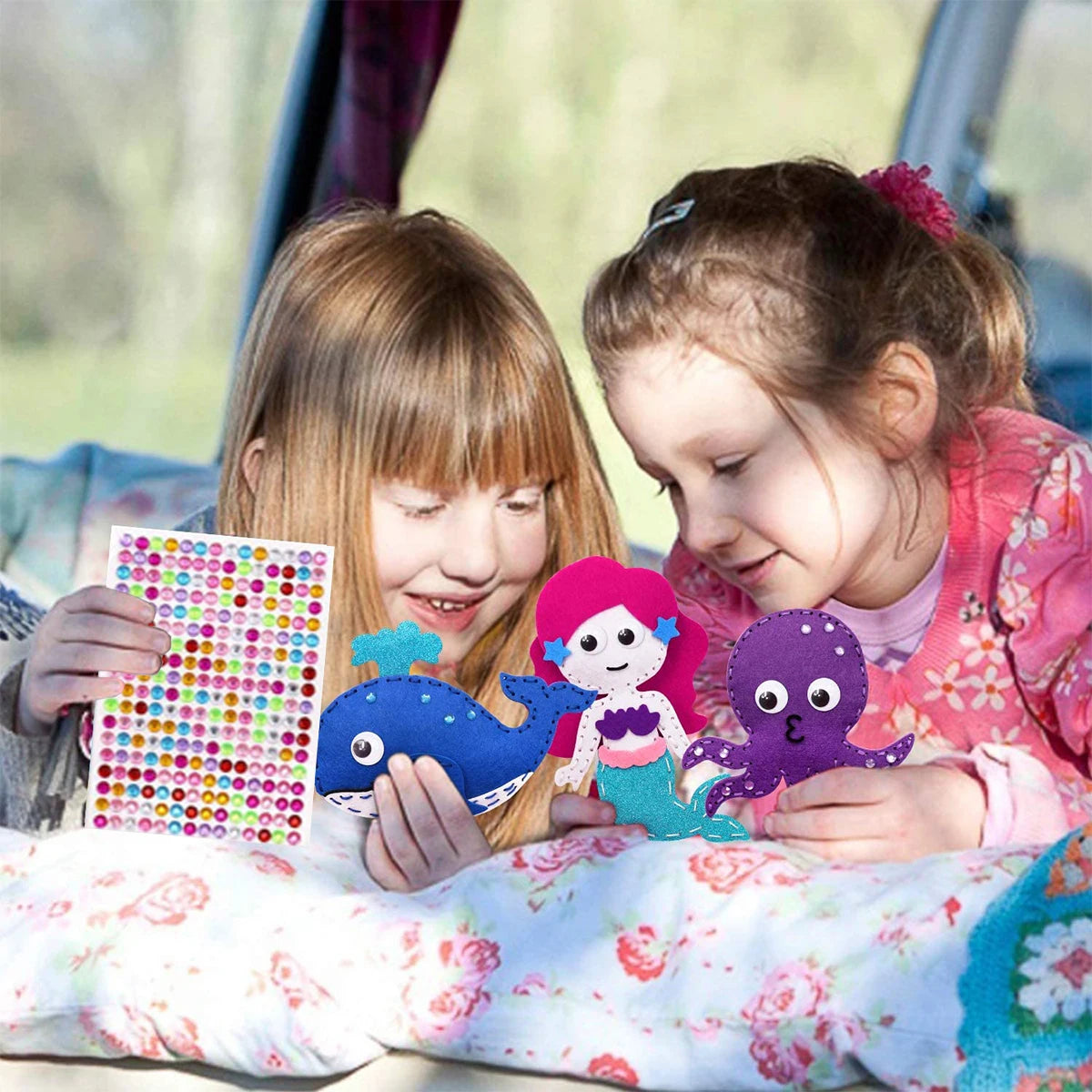 Two young girls are looking at and interacting with a felt sewing kit featuring woodland animals.