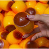 A hand is squeezing a squishy pudding stress ball fidget toy with bright yellow and orange colors.