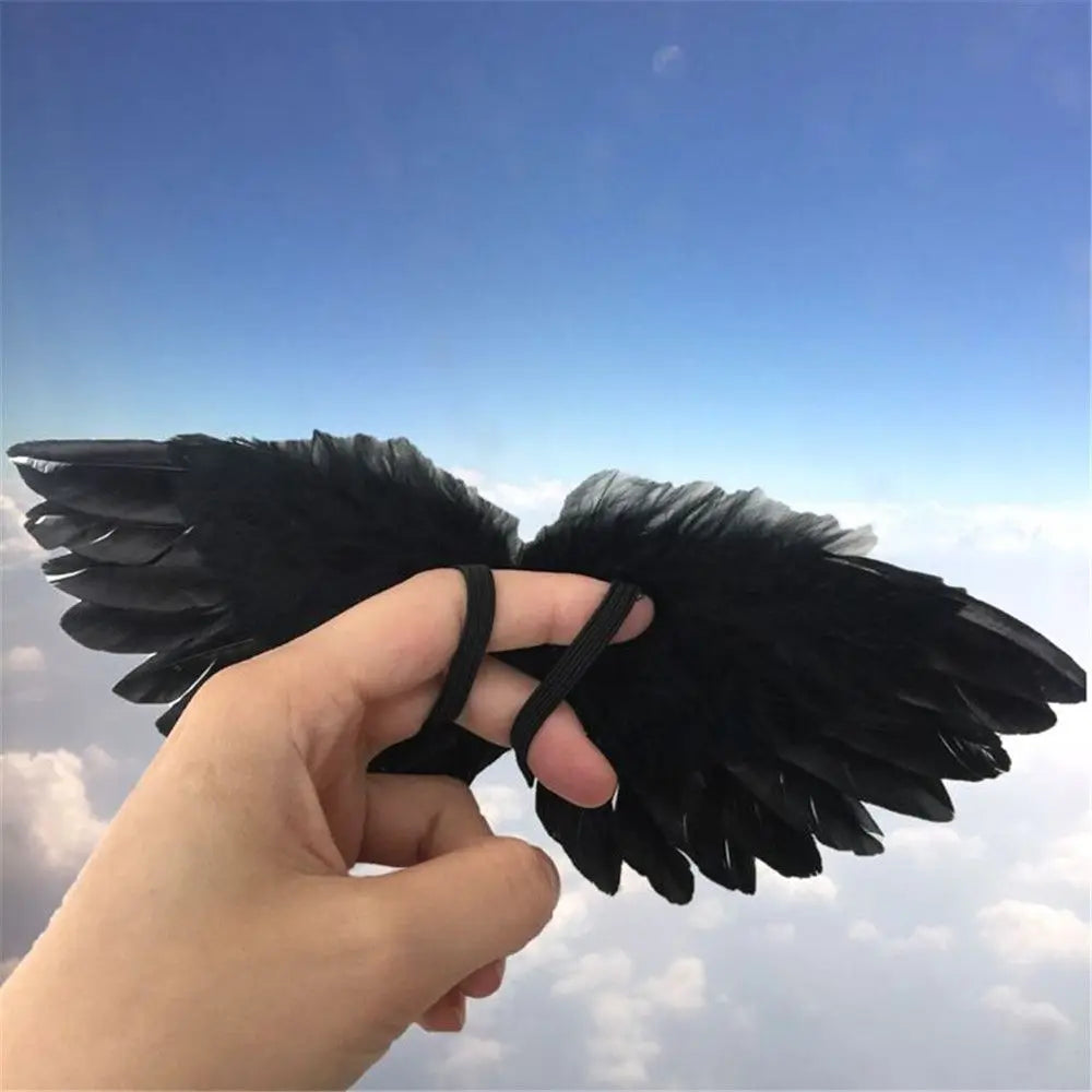 A hand holds a pair of black mini feather angel wings against a clear blue sky.