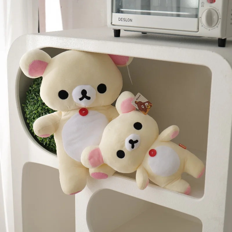 A pair of soft, light yellow Rilakkuma anime plush bears with pink accents displayed in a white shelf.