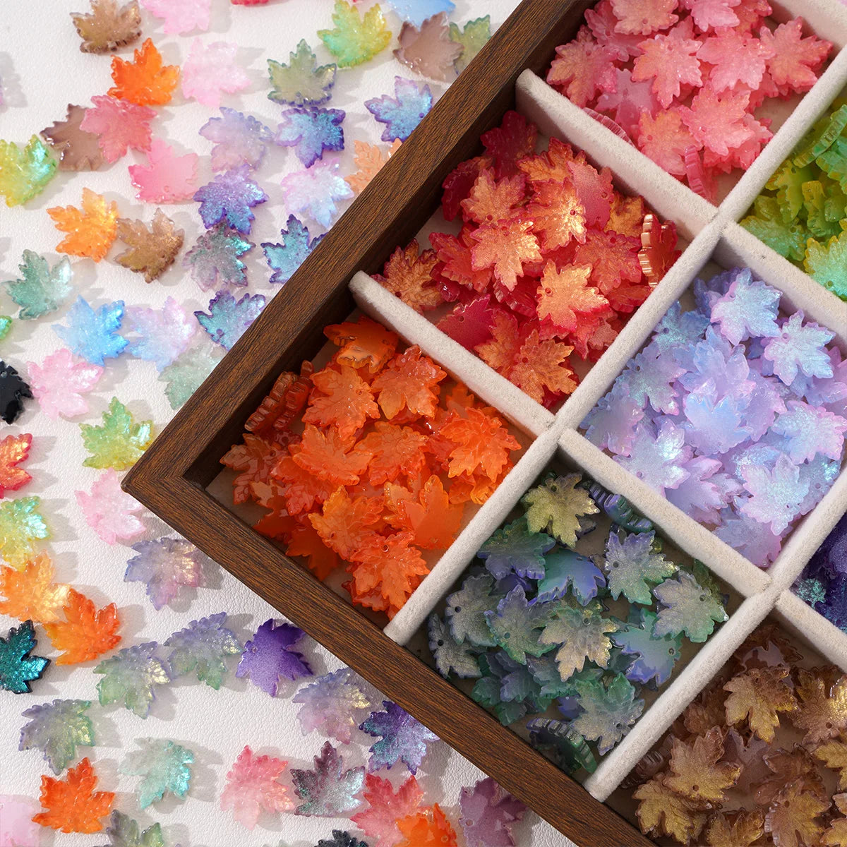 A wooden box filled with various colored maple leaf glass beads for DIY jewelry making