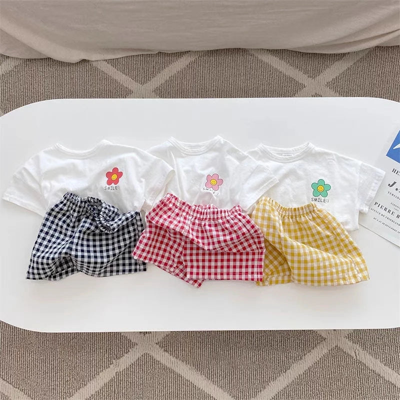 A flat lay of a floral print girls' summer t-shirt and shorts set in various patterns like plaid, gingham, and yellow stripes