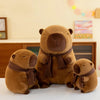 A brown plush capybara stuffed animal wearing a brown knit scarf sitting on a white surface.