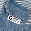Close-up of a light blue striped denim jacket showing a sewn-in tag with a black G design.