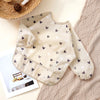 A beige waterproof long sleeve feeding bib with a subtle pattern of gray and black hearts is displayed on a textured fabric.