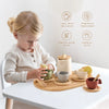 A young girl is playing with a wooden pretend tea party set, demonstrating social skills and imagination.