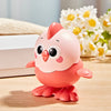 A pink wind-up chick toy with a pull chain sitting on a wooden surface next to white boxes and white flowers.