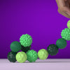 A hand is holding a string of green silicone massage balls with magnetic cores against a purple background.