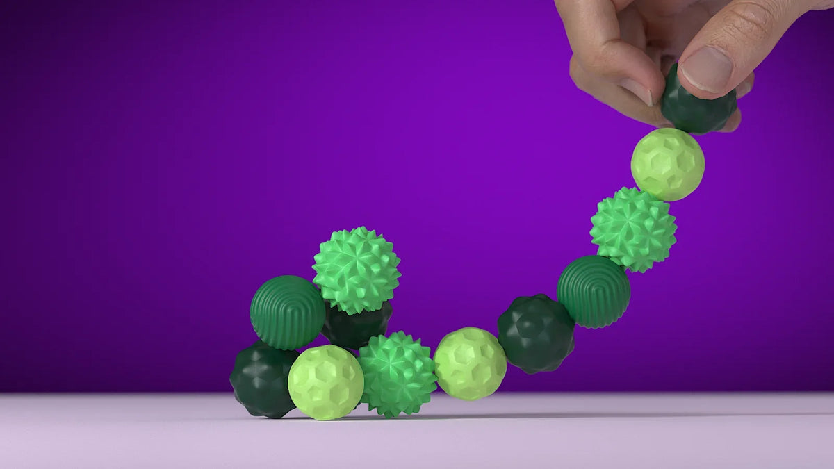 A hand is holding a string of green silicone massage balls with magnetic cores against a purple background.
