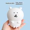 A white silicone lamp shaped like a bear is held in a hand, described as gentle on skin, soft, chewy, and bouncy.