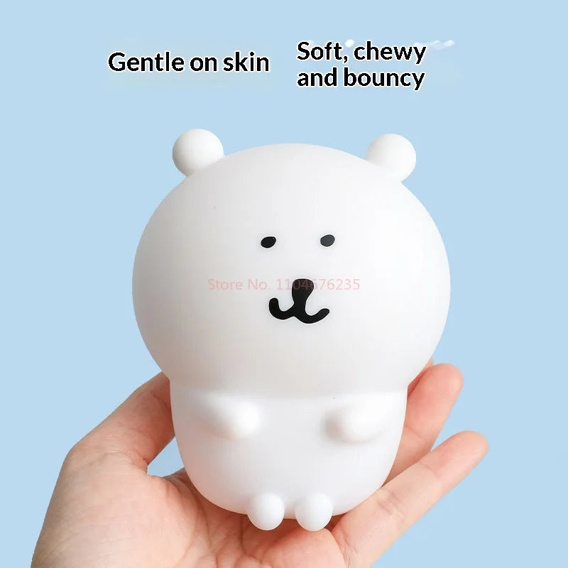 A white silicone lamp shaped like a bear is held in a hand, described as gentle on skin, soft, chewy, and bouncy.