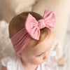 A baby wearing a pink fabric headband with a large bow, looking down.