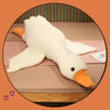 A white plush goose pillow with an orange beak lying on a wooden surface.
