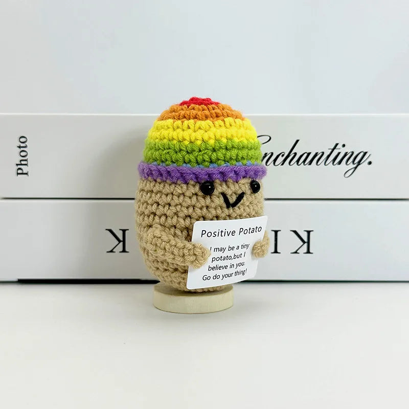 A handwoven crochet pencil ornament shaped like a potato with colorful yarn hair and a small sign.