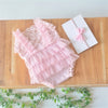 Pink lace baby romper with ruffled trim and a matching pink fabric headband displayed on a wooden surface.