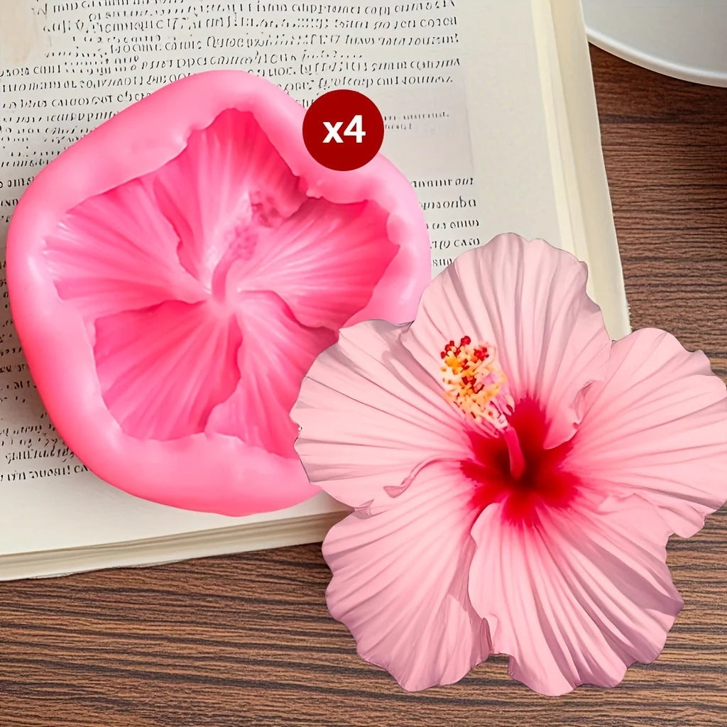 Four pink hibiscus flower silicone molds are displayed on a wooden surface next to an open book.