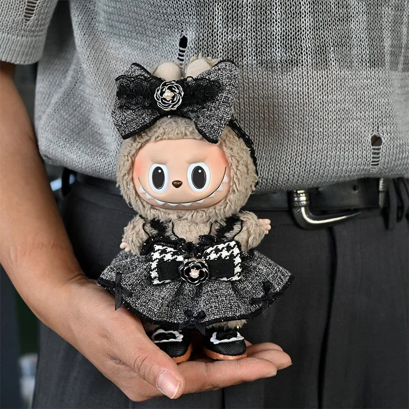 A small, fluffy doll wearing a black and white flannel outfit with a bow is held in a person's hand.