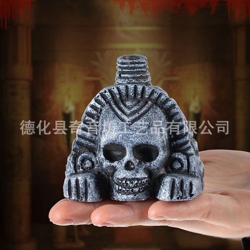 A hand holds a dark gray stone sculpture of an Aztec death whistle skull with intricate facial details.