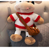 A plush cow stuffed animal with white and red accents sitting on a gray upholstered surface.