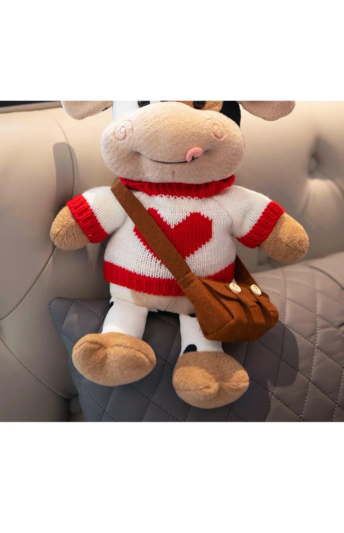 A plush cow stuffed animal with white and red accents sitting on a gray upholstered surface.