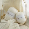 A ball of white wool yarn is displayed in a woven basket with a knitted sample and a book.