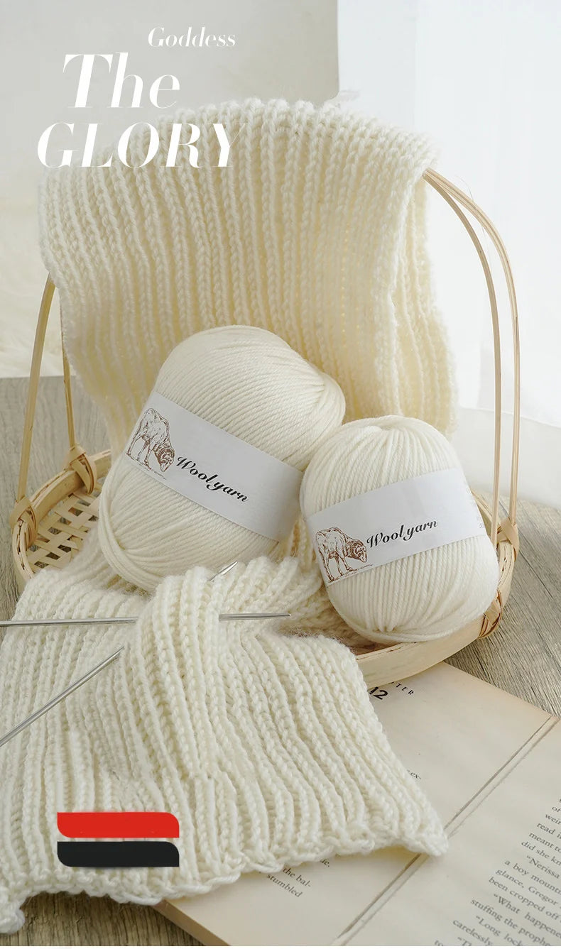 A ball of white wool yarn is displayed in a woven basket with a knitted sample and a book.