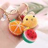 Handmade crochet fruit keychain pendants in orange, yellow, and green colors displayed on a hand.