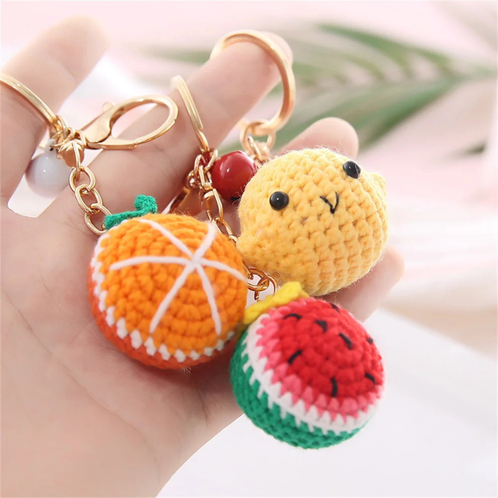 Handmade crochet fruit keychain pendants in orange, yellow, and green colors displayed on a hand.