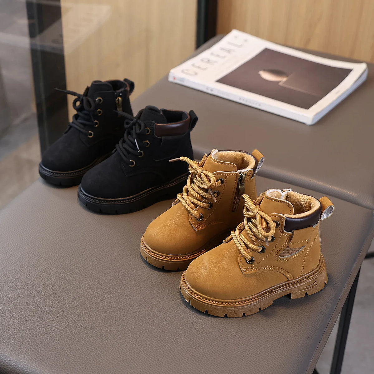 A pair of tan leather winter boots with laces and a brown cuff resting on a gray table.