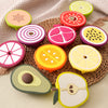 A collection of silicone baby teethers shaped like various fruits and vegetables in bright colors, resting on a woven mat.