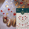 A close-up of gold and red heart nail art stickers on a translucent surface with nail tips.