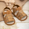 A pair of tan soft non-slip baby sandals for first walkers resting on a light wooden surface.