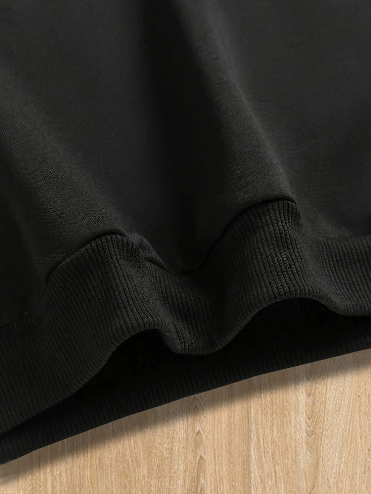 A close-up of a black pullover hoodie with ribbed cuffs and a letter print detail.
