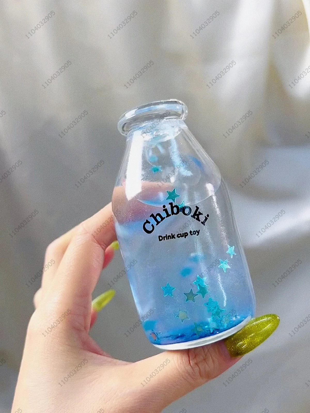 A hand holds a clear blue plastic bottle filled with liquid and decorated with star-shaped confetti, identified as a chibi dr