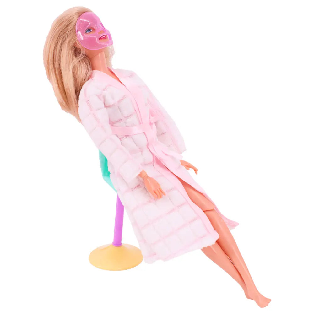 A blonde doll wearing a pink coat and a pink mask is shown with a cleaning accessory stand.
